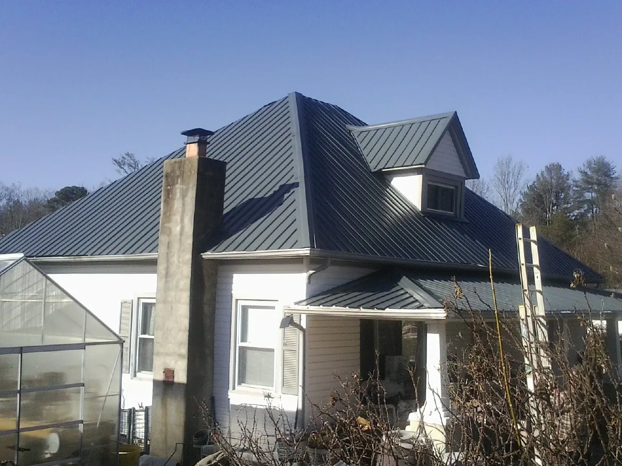 Dark blue standing seam metal roof on a white farmhouse with dormer — Slate & Tile Roof Repair by Roofing Brothers in Hankins