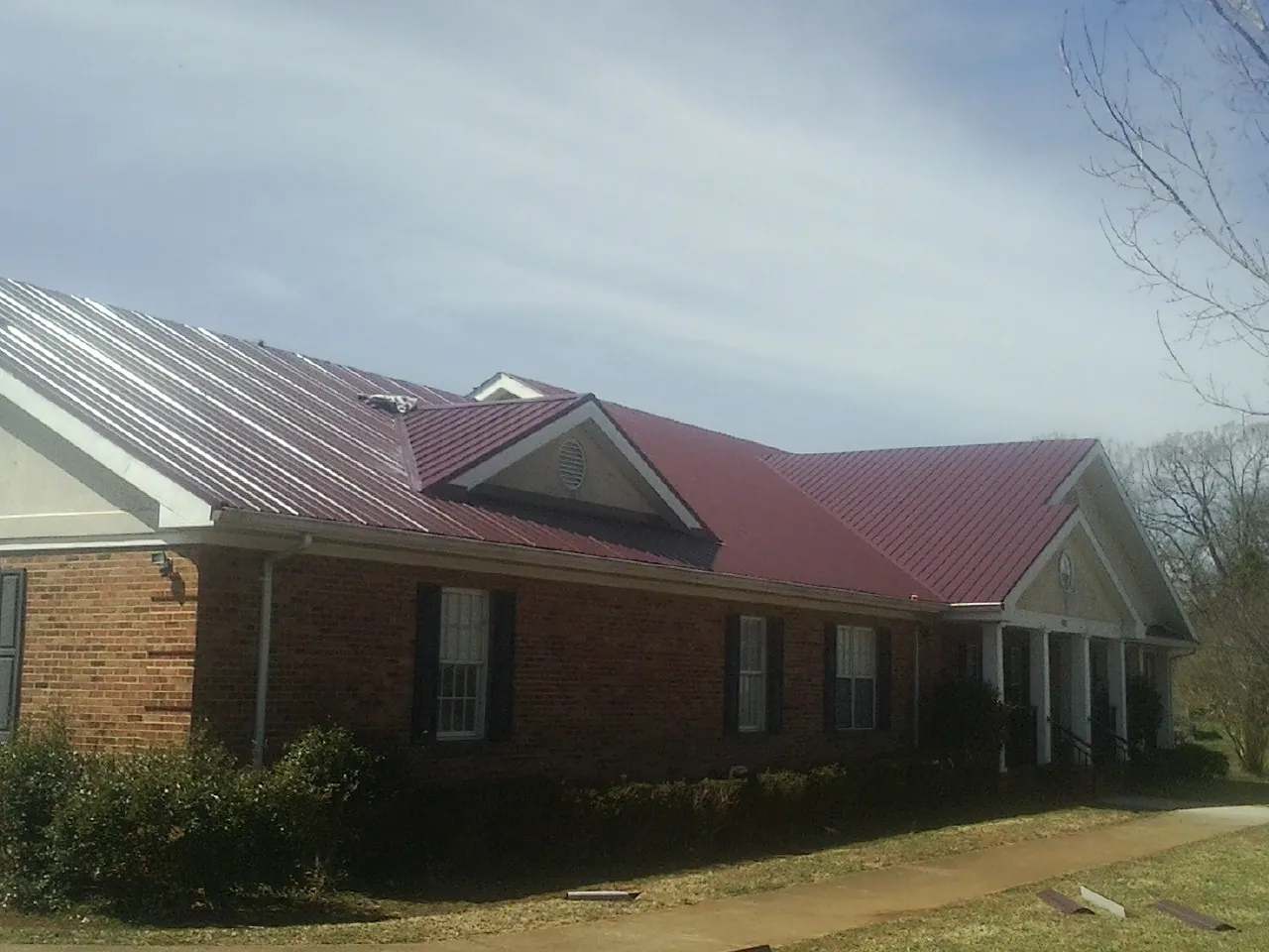 Red metal roof with gabled entries on a long brick building, from a Hail Damage Roof Repair job in Hankins