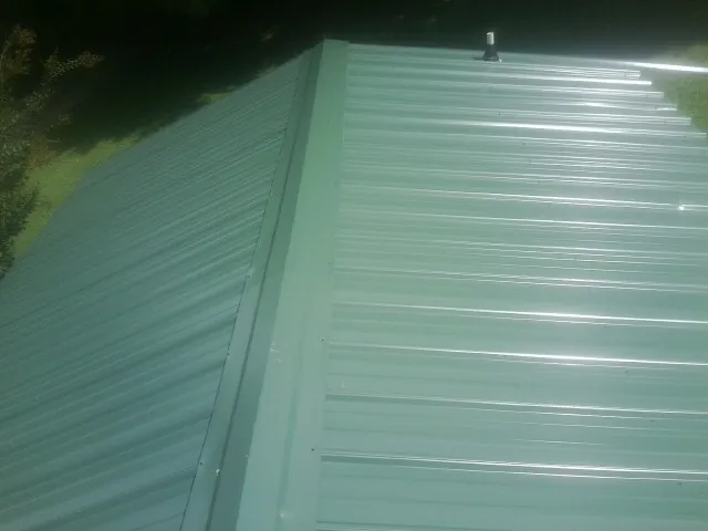 New green metal panels meeting at the ridge of a roof — Flat Roof Repair work by our crew in Hankins