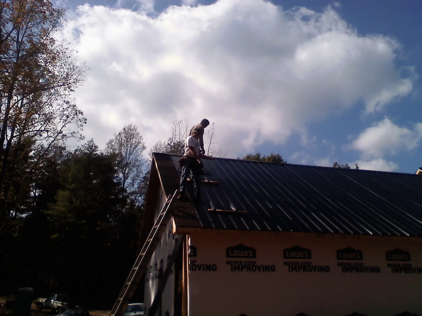 Roofer fastening dark metal panels high against a cloudy sky, from a Roof Inspection job in Hankins
