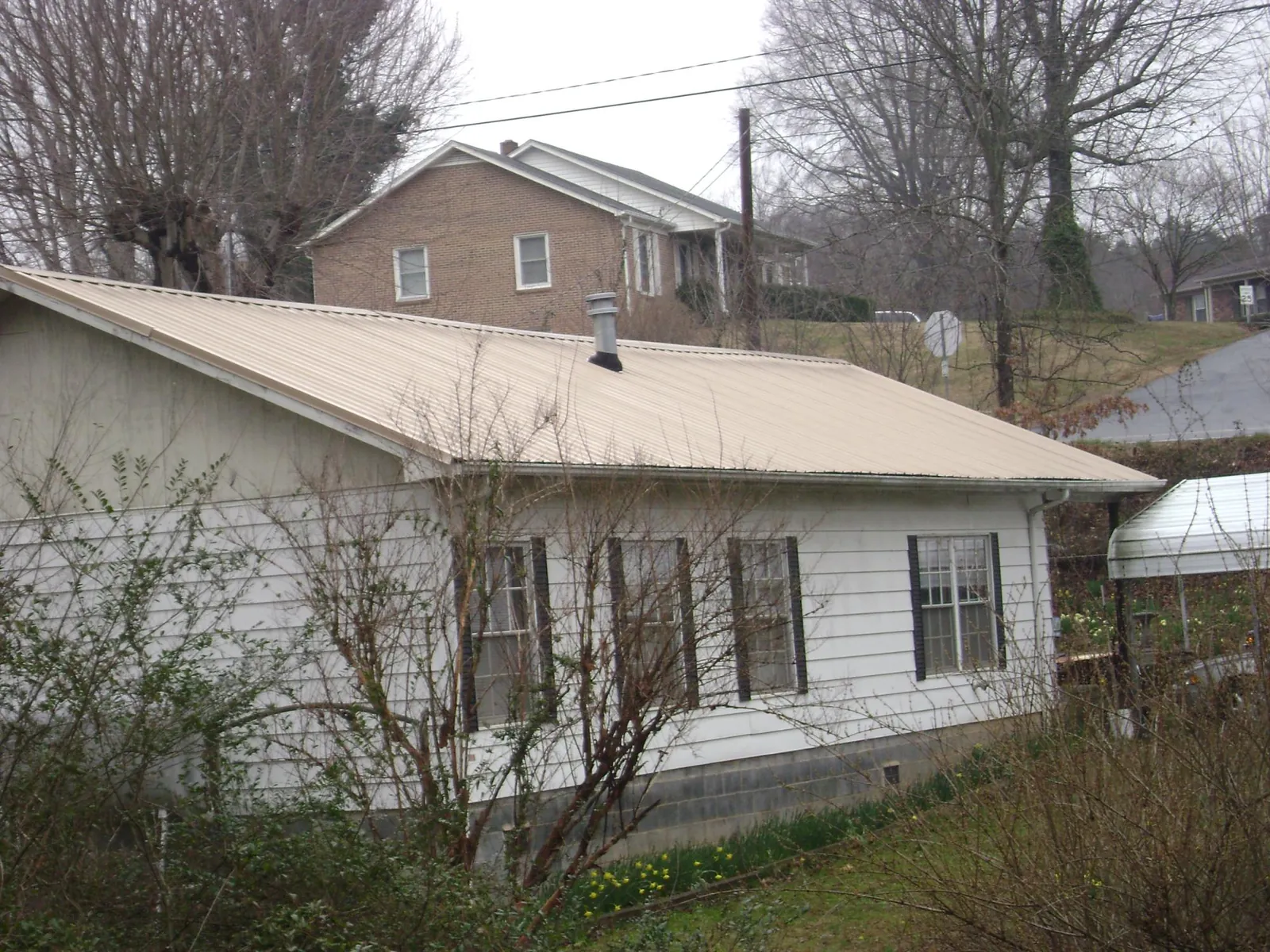Tan metal roof on a white sided house set into a hillside — Commercial Roofing by Roofing Brothers in Hankins