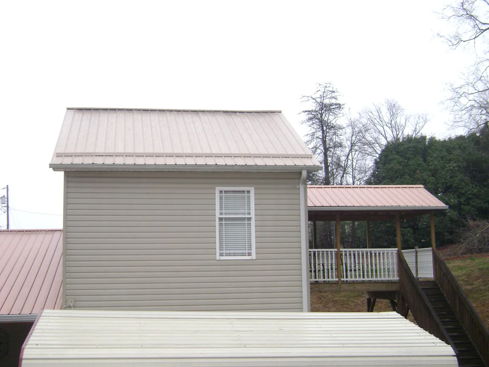 Tan metal roofs on a two story addition and attached porch, from a Roof Replacement job in Hankins